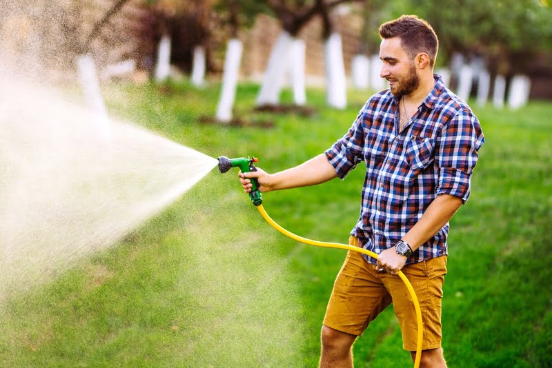 Mann bewässert Rasen mit Schlauch